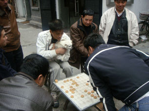 Chess players in a small street. One is holding his dog